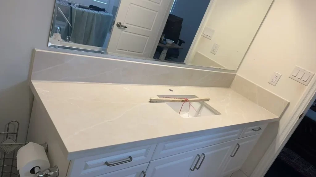 Bathroom vanity with warm cream ivory quartz countertop subtle gold veining rectangular undermount sink white raised panel cabinet doors brushed nickel hardware and large frameless mirror by MD Kitchen and Bath