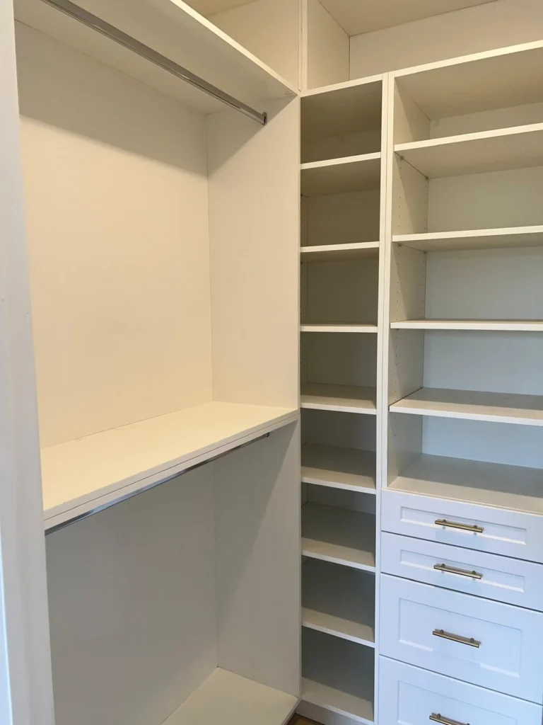 Custom white walk-in closet interior with hanging rod section open shelving tower and three drawer unit with brushed nickel bar pull hardware