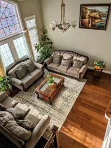 Aerial view of traditional living room with warm medium oak hardwood flooring grey beige traditional sofa set glass top wood coffee table stained glass window and chandelier overhead