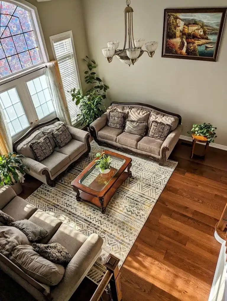 Aerial view of traditional living room with warm medium oak hardwood flooring grey beige traditional sofa set glass top wood coffee table stained glass window and chandelier overhead by MD Kitchen and Bath
