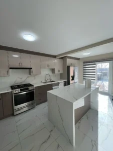After photo of renovated kitchen showing GE stainless gas range two tone high gloss taupe cabinets calacatta quartz countertop and island marble porcelain tile floor and zebra roller blinds