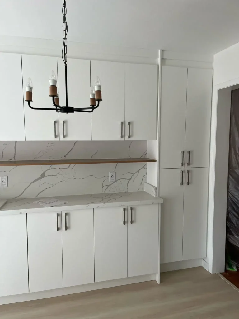 After photo of renovated kitchen featuring white flat panel slab upper and lower cabinets calacatta quartz countertop and full height backsplash wood floating open shelf brushed nickel bar pulls black iron candle chandelier and light gray LVP flooring