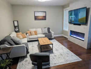 Modern living room with floor to ceiling Calacatta quartz electric fireplace feature wall wall mounted TV white sectional sofa wood and metal coffee table patterned area rug and dark hardwood floor