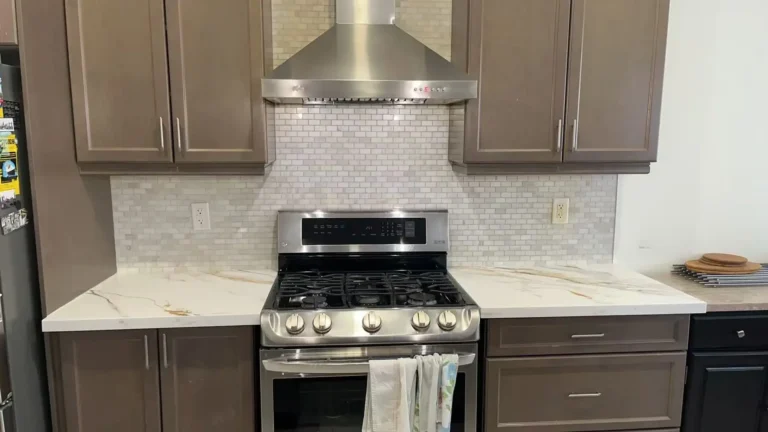 Taupe brown shaker kitchen range wall with stainless 5-burner gas range gold knobs stainless chimney hood white mini subway tile backsplash and Calacatta gold quartz countertop with bold gold and white veining by MD Kitchen and Bath