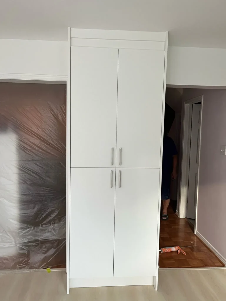 Tall white floor to ceiling pantry cabinet with four smooth panel doors and brushed nickel bar pulls freshly installed with parquet hardwood flooring below by MD Kitchen and Bath