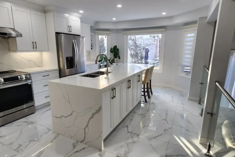 After photo of renovated kitchen taken from staircase angle showing LG stainless gas range white shaker cabinets calacatta quartz island and countertops matching quartz backsplash stainless range hood glass panel railing and marble porcelain tile floor