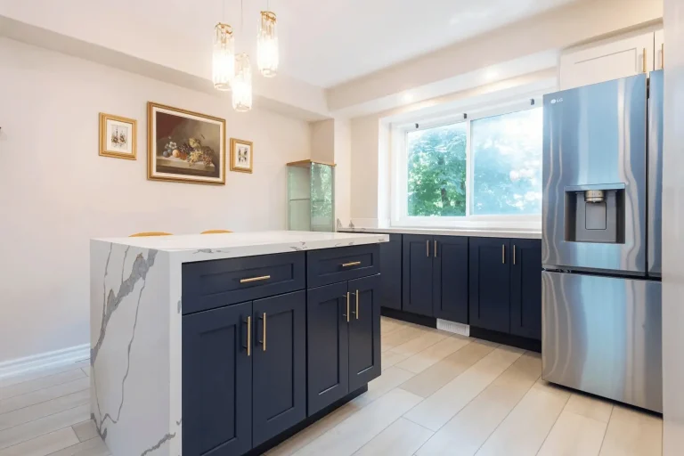 Navy blue shaker lower cabinets and island with brushed gold bar pulls calacatta quartz waterfall island top white upper shelving unit LG stainless French door refrigerator with water dispenser crystal drop pendant light light wood look porcelain tile floor and framed artwork on wall