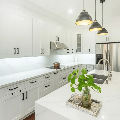 Two tone kitchen with white shaker upper cabinets and gray shaker lower cabinets matte black bar pulls calacatta quartz island with stainless undermount sink brushed nickel gooseneck faucet three dark dome pendant lights stainless range hood stainless French door refrigerator and dark hardwood flooring