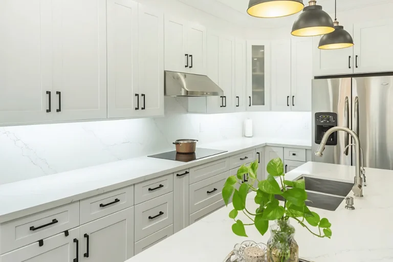Two tone kitchen with white shaker upper cabinets and gray shaker lower cabinets matte black bar pulls calacatta quartz island with stainless undermount sink brushed nickel gooseneck faucet three dark dome pendant lights stainless range hood stainless French door refrigerator and dark hardwood flooring