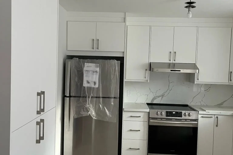 Full view of white flat panel kitchen with floor to ceiling pantry column stainless Whirlpool refrigerator Frigidaire range under cabinet hood Calacatta quartz countertop and backsplash and light oak LVP flooring by MD Kitchen and Bath