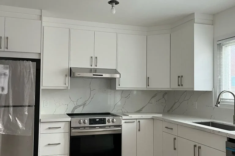 Wide view of white flat panel L-shape kitchen with Calacatta quartz countertops and backsplash stainless undermount sink brushed nickel faucet Frigidaire range under cabinet hood and light oak LVP flooring by MD Kitchen and Bath