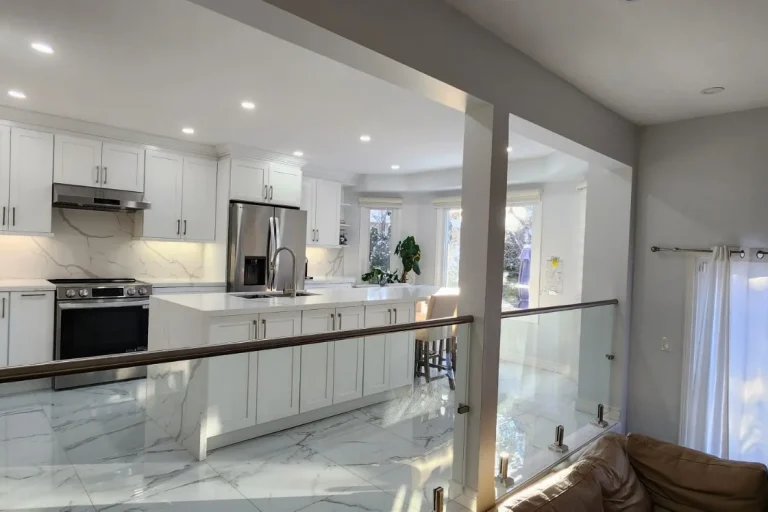 Luxury all-white kitchen renovation viewed from hallway glass railing with large quartz island and marble tile floor by MD Kitchen and Bath