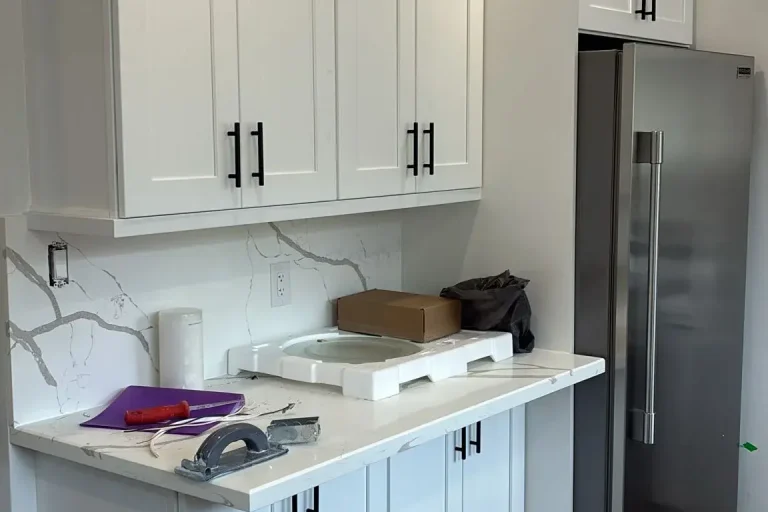 White shaker kitchen fridge wall with stainless side by side refrigerator white shaker upper cabinets matte black bar pull hardware Calacatta quartz countertop and backsplash and grey LVP flooring by MD Kitchen and Bath