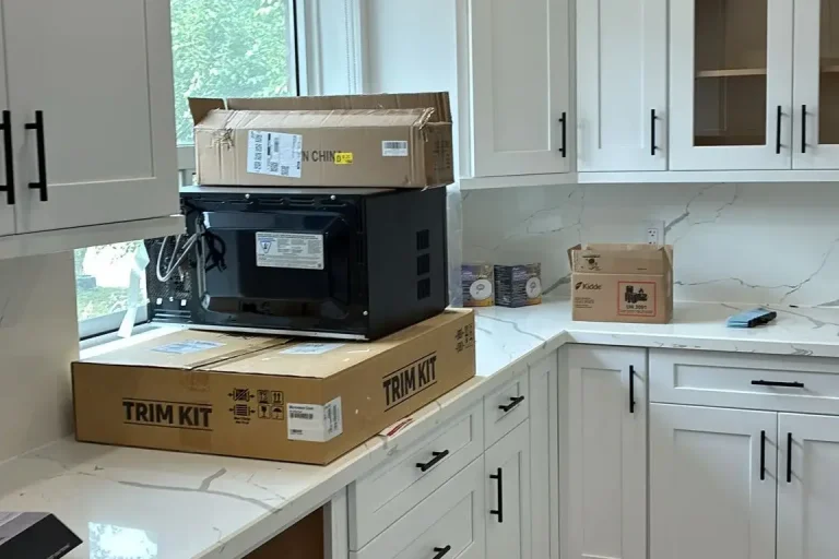 Full view of white shaker kitchen with glass front upper cabinet matte black bar pull hardware Calacatta quartz countertop and backsplash and grey LVP flooring by MD Kitchen and Bath