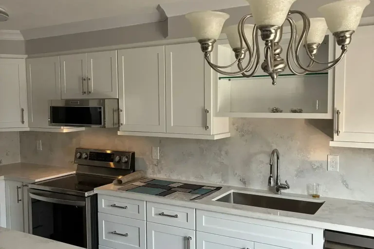 Full wall view of white shaker kitchen with brushed nickel hardware cloud grey quartz backsplash white quartz countertop stainless range stainless built-in microwave stainless undermount sink stainless dishwasher silver chandelier and dark charcoal island in foreground by MD Kitchen and Bath