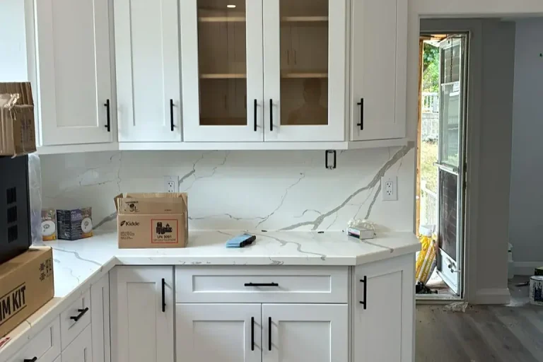 White shaker kitchen corner with glass front upper cabinet matte black bar pull hardware Calacatta quartz countertop and backsplash angled corner base cabinet and grey LVP flooring by MD Kitchen and Bath