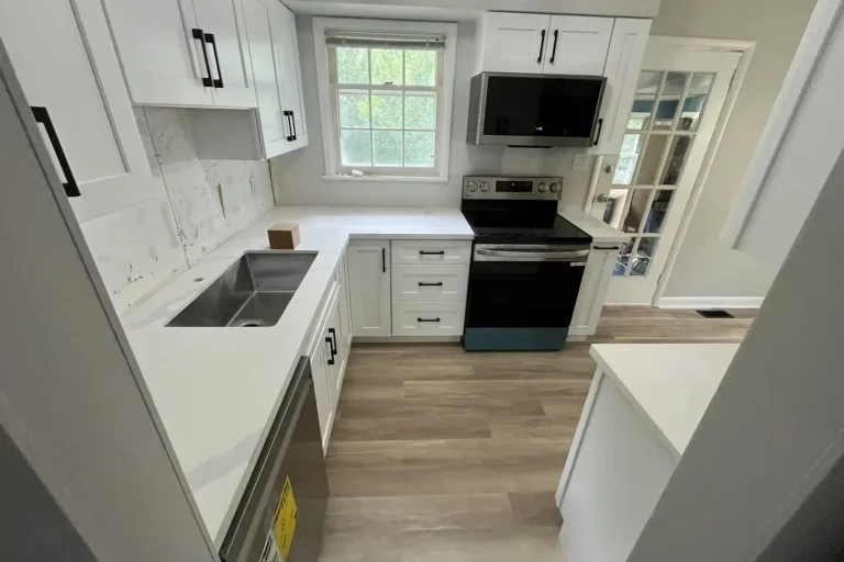 White shaker U-shape kitchen with matte black bar pull hardware Calacatta quartz countertop and backsplash stainless undermount sink Frigidaire range Samsung over the range microwave and light oak LVP flooring by MD Kitchen and Bath