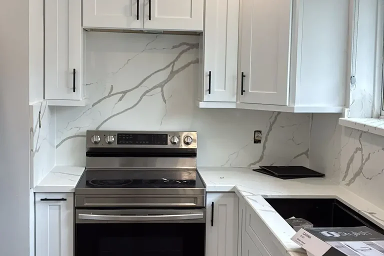 White shaker kitchen range wall with matte black bar pull hardware stainless electric range Calacatta quartz countertop and full height backsplash and grey LVP flooring by MD Kitchen and Bath