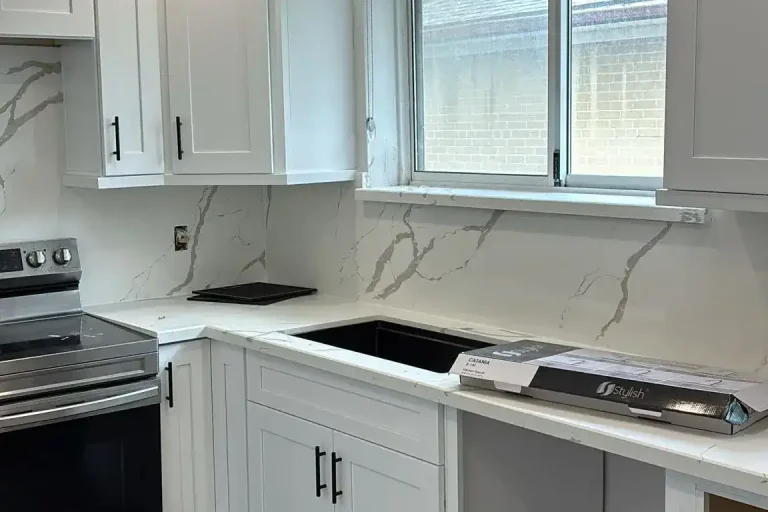 White shaker kitchen sink wall with matte black bar pull hardware Calacatta quartz countertop and full height backsplash stainless electric range grey LVP flooring and roller blind window by MD Kitchen and Bath