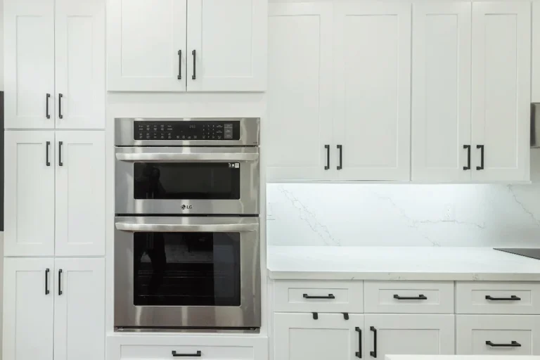White shaker upper and lower cabinets with tall floor to ceiling pantry cabinet surround matte black bar pulls LG stainless double wall oven calacatta quartz countertop and backsplash and dark hardwood flooring